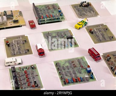 Les véhicules miniatures d'urgence et de service naviguent sur une grille de rue formée par des cartes de circuits électroniques, illustrant l'infrastructure technologique, les réseaux, Banque D'Images