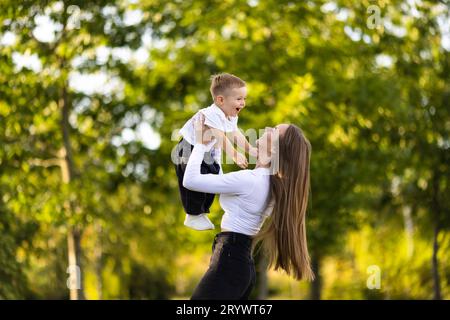 Jeune belle mère joue avec son bébé à l'extérieur. La famille heureuse et aimante mère et son petit fils jouent et embrasent tout en célébrant la mère Banque D'Images