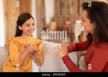 Heureuse fille d'enfant apprenant la langue des signes avec la dame tuteur à l'intérieur Banque D'Images