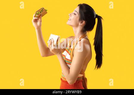 Jeune femme avec des sandwichs savoureux sur fond jaune Banque D'Images