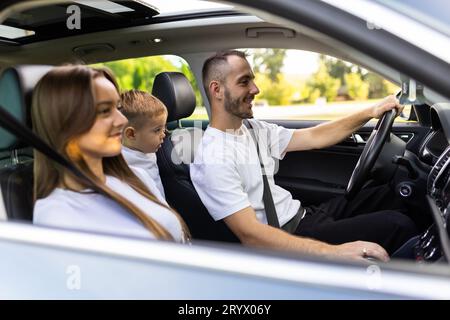 Joyeux jeune famille traditionnelle a un long voyage d'auto et de chanter à haute voix la chanson préférée ensemble. Concept de voiture de sécurité grand angle intérieur env Banque D'Images