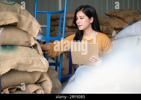 Jeune femme asiatique assise sur le sol dans l'entrepôt de grains de café et vérifiant les documents Banque D'Images