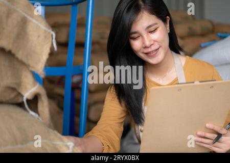 Jeune femme asiatique assise sur le sol dans l'entrepôt de grains de café et vérifiant les documents Banque D'Images