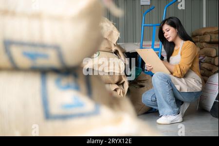 Jeune femme asiatique assise sur le sol dans l'entrepôt de grains de café et vérifiant les documents Banque D'Images