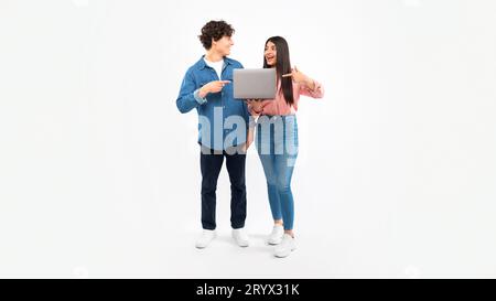 Couple tenant l'ordinateur portable pointant les doigts vers l'ordinateur sur le fond blanc Banque D'Images