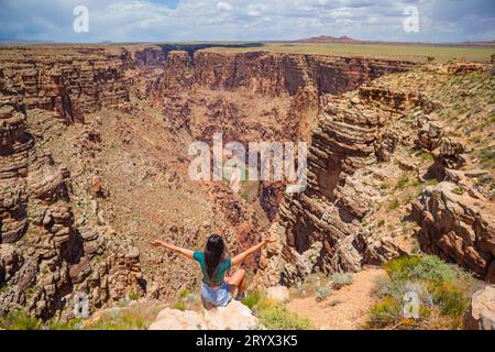 Heureuse jeune femme sur une falaise escarpée prenant dans la vue imprenable sur le célèbre Grand Canyon sur une belle journée ensoleillée, Grand Canyon Na Banque D'Images