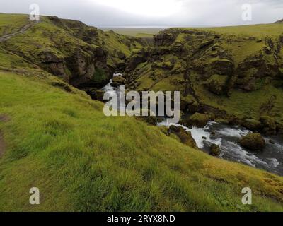 Vue panoramique d'une cascade coulant entre les falaises d'herbe sous un ciel gris Banque D'Images