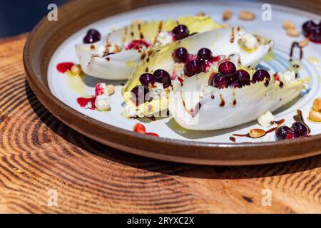 Hors-d'œuvre végétariens préparés avec des bateaux d'endives belges frais farcis de pignons grillés, fromage bleu, baies de porc fraîches et huile d'olive fraîche garnie Banque D'Images