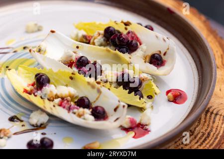 Hors-d'œuvre végétariens préparés avec des bateaux d'endives belges frais farcis de pignons grillés, fromage bleu, baies de porc fraîches et huile d'olive fraîche garnie Banque D'Images