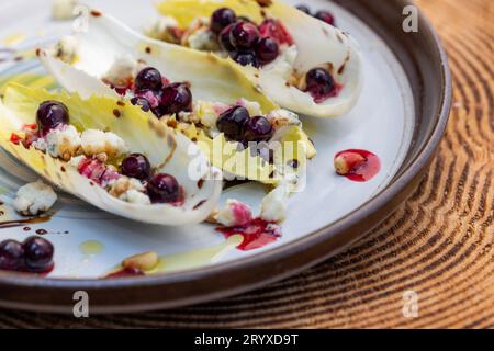 Hors-d'œuvre végétariens préparés avec des bateaux d'endives belges frais farcis de pignons grillés, fromage bleu, baies de porc fraîches et huile d'olive fraîche garnie Banque D'Images