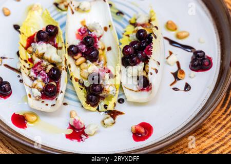 Hors-d'œuvre végétariens préparés avec des bateaux d'endives belges frais farcis de pignons grillés, fromage bleu, baies de porc fraîches et huile d'olive fraîche garnie Banque D'Images