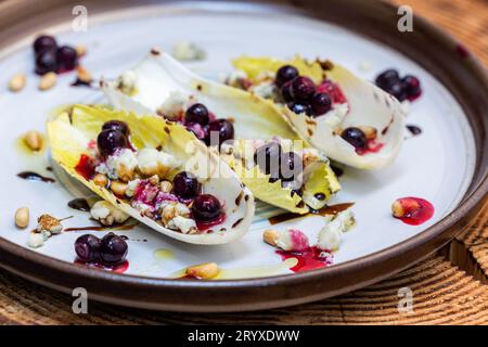 Hors-d'œuvre végétariens préparés avec des bateaux d'endives belges frais farcis de pignons grillés, fromage bleu, baies de porc fraîches et huile d'olive fraîche garnie Banque D'Images