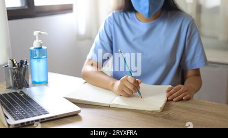 Jeune femme asiatique portant un masque médical facial fait à la main travaillant aloneÂ dans la politique de distanciation avec. Désinfectant pour les mains gelÂ pendant coronav Banque D'Images