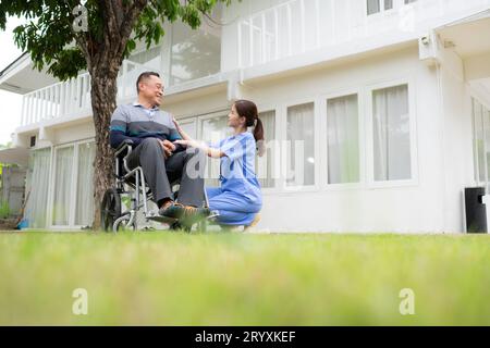 Infirmière souriante et homme âgé assis dans un fauteuil roulant dans le jardin Banque D'Images