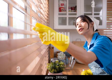 Jeune femme asiatique nettoyant la fenêtre dans la cuisine. concept de travaux ménagers Banque D'Images