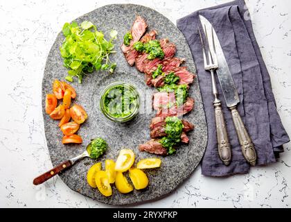 Tranches de steak de boeuf avec sauce au chimmichuri sur plaque de pierre grise Banque D'Images