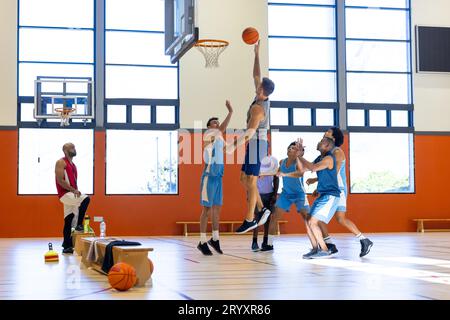 Divers joueurs de basket-ball masculins portant des vêtements de sport bleus et jouant au basket-ball avec entraîneur à la salle de gym Banque D'Images