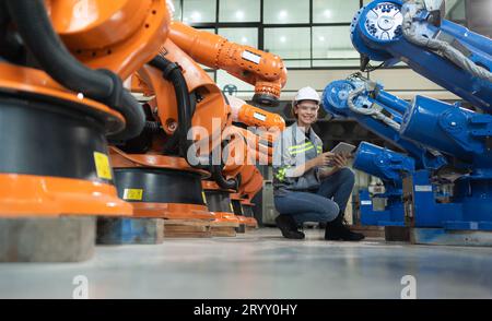 Une ingénieure installe un programme sur un bras robotique dans un entrepôt de robots. Et tester l'opération avant d'envoyer la machine t Banque D'Images