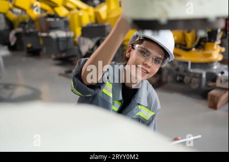 Une ingénieure installe un programme sur un bras robotique dans un entrepôt de robots. Et tester l'opération avant d'envoyer la machine t Banque D'Images