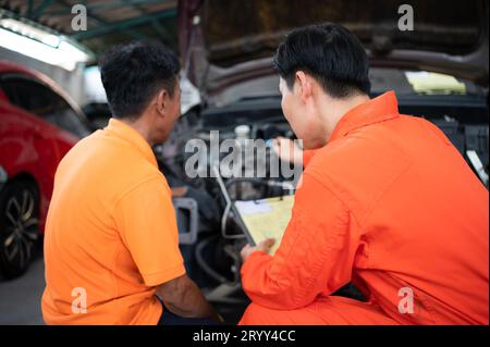 Les deux mécaniciens inspectent le moteur de la voiture d'un client qui est amené pour réparation dans un garage. Banque D'Images