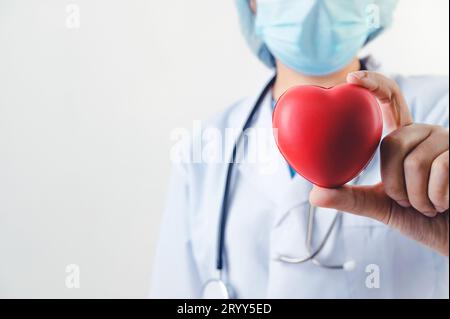Gros plan du cœur rouge dans la main du médecin avec stéthoscope sur fond blanc. Concept de personnel médical et de cardio-praticien. Cœur Banque D'Images