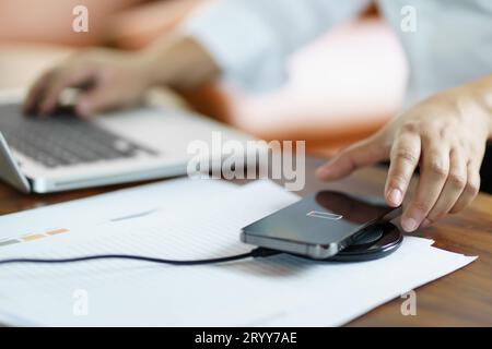 Chargement de la batterie du téléphone portable avec le dispositif de chargement sans fil dans la table. Chargement du smartphone sur un plateau de chargement. Téléphone portable ne Banque D'Images