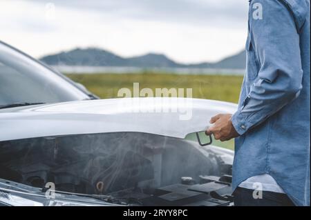 Capot de voiture ouvert homme asiatique pour la réparation en tant que service d'entretien avec fond de paysage entre long voyage sur la route. Voiture cassée et cassée Banque D'Images