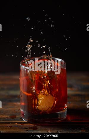 Cocktail alcoolisé Negroni ou cocktail non alcoolisé avec éclaboussure dans le verre, boire avec de la glace et de l'écorce d'orange comme décoration sur woode Banque D'Images