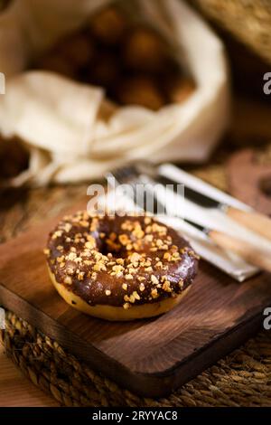 Un plan rapproché séduisant d'un beignet sur une planche de bois. Serviette blanche, couverts en bois et noix décortiquées en arrière-plan ajoutent un charme rustique. Banque D'Images