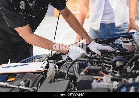 Le mécanicien automobile masculin asiatique examine le problème de panne de moteur de voiture devant le capot de voiture de véhicule automobile avec le client féminin. Sûr Banque D'Images