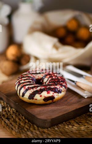 Un plan rapproché séduisant d'un beignet sur une planche de bois. Serviette blanche, couverts en bois et noix décortiquées en arrière-plan ajoutent un charme rustique. Banque D'Images