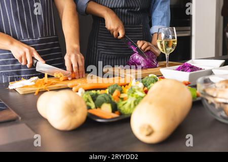 Section médiane de divers couples dans des tabliers préparant le repas, hachant les légumes dans la cuisine Banque D'Images
