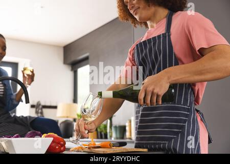 Heureux couple diversifié préparant le repas et buvant du vin dans la cuisine Banque D'Images