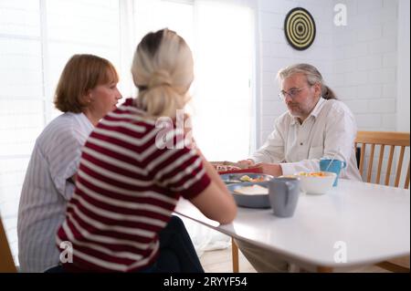 Le père, la mère et la fille sont ravis de dîner ensemble à la table familiale. Banque D'Images