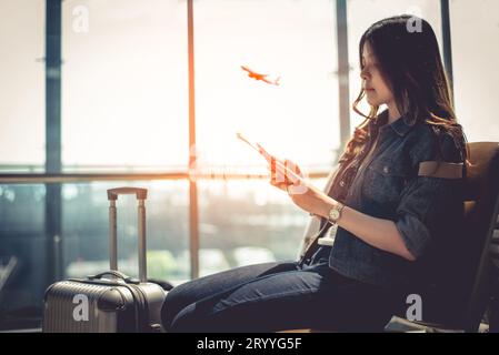 Femme asiatique de beauté avec bagage valise en attente pour le départ tout en utilisant un téléphone intelligent dans le salon de l'aéroport. Voyageur féminin et à Banque D'Images