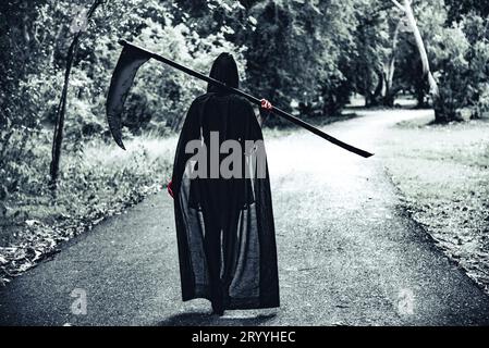 Vue arrière de sorcière démon avec faucheuse et sang rouge sur les mains marchant le long du fond de la route. Concept horreur et fantôme. Hallowe Banque D'Images