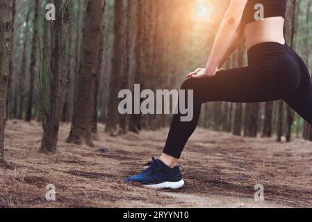 Gros plan du bas du corps d'une femme faisant du yoga et étirant les jambes avant de courir dans la forêt à l'extérieur. Concept Sport et nature. Banque D'Images