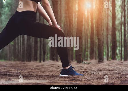 Gros plan du bas du corps d'une femme faisant du yoga et étirant les jambes avant de courir dans la forêt à l'extérieur. Concept Sport et nature. Banque D'Images