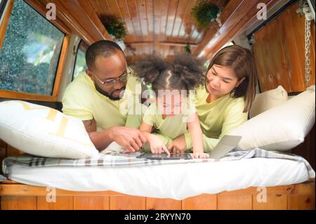 À l'arrière d'un van blanc classique, les petits enfants jouent et apprennent le monde sur leur tablette avec les parents qui s'occupent de les aider. Banque D'Images