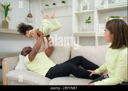 Parent s'amusant avec sa fille en vomissant et en la soulevant pendant que la mère est à côté. Banque D'Images