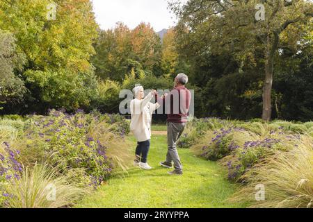 Heureux couple biracial senior dansant avec des fleurs autour d'eux dans le jardin à la maison Banque D'Images