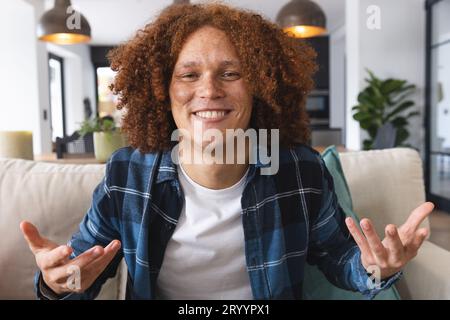 Heureux homme biracial ayant un appel vidéo assis sur le canapé, faisant des gestes et souriant dans le salon, à la maison Banque D'Images