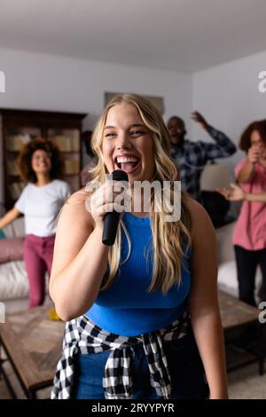 Heureux et divers amis dansant et chantant karaoké avec microphone à la maison Banque D'Images