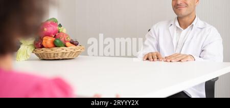 Médecin nutritionniste hispanique consultant un enfant métis avec sa mère afro-américaine au sujet d'une nutrition. Nourriture de légumes - une nouvelle façon pour le bien Banque D'Images