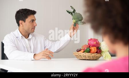 Médecin nutritionniste hispanique consultant un enfant métis avec sa mère afro-américaine au sujet d'une nutrition. Nourriture de légumes - une nouvelle façon pour le bien Banque D'Images