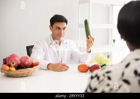 Médecin nutritionniste hispanique consultant un enfant métis avec sa mère afro-américaine au sujet d'une nutrition. Nourriture de légumes - une nouvelle façon pour le bien Banque D'Images