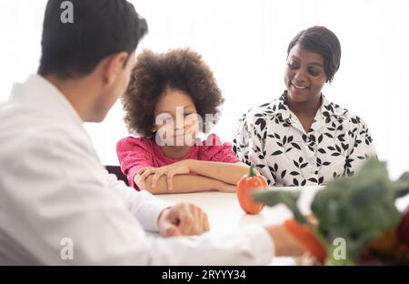 Médecin nutritionniste hispanique consultant un enfant métis avec sa mère afro-américaine au sujet d'une nutrition. Nourriture de légumes - une nouvelle façon pour le bien Banque D'Images