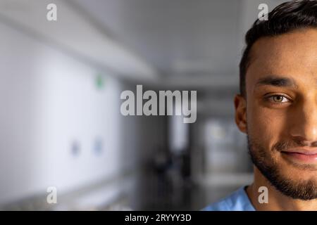 Portrait d'un médecin homme biracial heureux portant des gommages dans le couloir à l'hôpital, espace de copie Banque D'Images