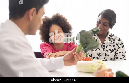 Médecin nutritionniste hispanique consultant un enfant métis avec sa mère afro-américaine au sujet d'une nutrition. Nourriture de légumes - une nouvelle façon pour le bien Banque D'Images