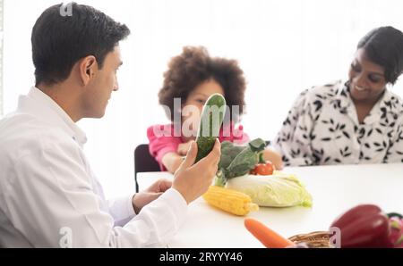 Médecin nutritionniste hispanique consultant un enfant métis avec sa mère afro-américaine au sujet d'une nutrition. Nourriture de légumes - une nouvelle façon pour le bien Banque D'Images